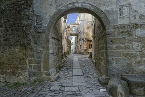Aussicht durch ein gewölbt Tor entlang ein Kopfsteinpflaster Straße in ein uralt Dorf ohne Menschen foto
