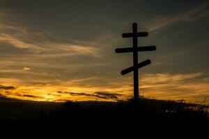 Kreuz auf oben von ein Hügel gegen ein Blau Himmel mit Weiß Wolken. Silhouette von ein Kreuz im das Feld beim Sonnenuntergang mit dramatisch Himmel. foto