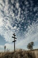 Kreuz auf oben von ein Hügel gegen ein Blau Himmel mit Weiß Wolken. Silhouette von ein Kreuz im das Feld beim Sonnenuntergang mit dramatisch Himmel. foto