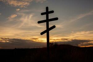 Kreuz auf oben von ein Hügel gegen ein Blau Himmel mit Weiß Wolken. Silhouette von ein Kreuz im das Feld beim Sonnenuntergang mit dramatisch Himmel. foto