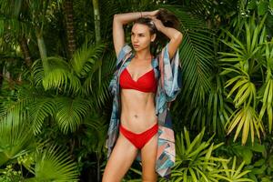 schön Frau Modell- im rot schwimmen tragen mit lange Gerade Haar posieren im tropisch Natur. perfekt bräunen Körper. foto