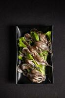 unglaublich gekocht Kraken mit Grün Salat auf ein schwarz Teller.chinesisch Küche, Hotpot Zutat foto