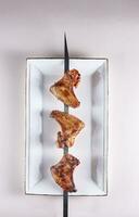 gebraten Hähnchen Flügel auf ein Spieß und ein Weiß Platte. Grill Chinesisch Küche foto