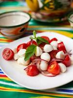 Caprese Salat mit Mazzarella Tomaten und Kräuter im orientalisch Stil auf ein Tabelle mit ein Teekanne und ein Tasse zum Tee. foto