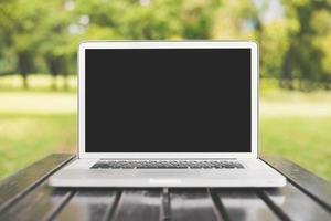 Laptop-Computer mit leerem schwarzem Bildschirm auf grünem Naturhintergrund