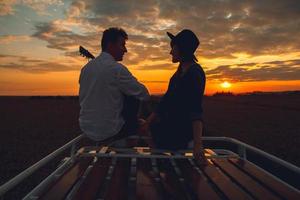 Silhouette von Mann mit Gitarre und Frau auf dem Dach eines Autos bei Sonnenuntergang foto