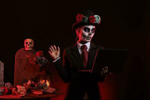 unheimlich Frau mit Laptop auf Dios de los Muertos Mexikaner Urlaub, feiern Tag von das tot mit Santa muerte Kostüm. tragen Göttin von Tod Schädel Körper Kunst, suchen beim kabellos Stk. foto