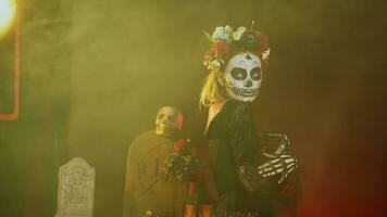 glamourös Frau mit Zucker Schädel machen oben und Blumen Stirnband, gekleidet im Göttin von Tod Kostüm wie Santa muerte. Dios de los Muertos Kunst zu feiern Mexikaner Tradition im Studio. Handheld Schuss. foto