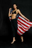 Porträt weiblich Athlet eingewickelt im amerikanisch Flagge gegen schwarz Hintergrund foto