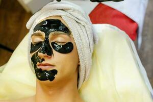 das Kosmetikerin setzt ein Maske auf das Gesicht von ein jung Mann. foto
