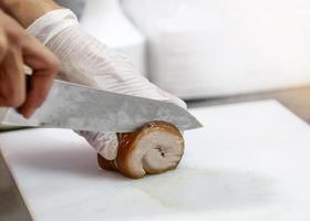 Koch schneidet Fleisch, Kochhände schneiden Bauchschweinefleisch gerolltes Gelenk foto
