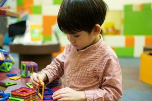 ein wenig asiatisch Junge ist spielen mit ein Platz magnetisch Puzzle. foto