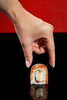 weiblich Hand nehmen Uramaki rollen mit angebraten Lachs, Sahne Käse, Tobiko und Apfel foto