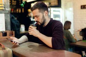 jung Hipster Kerl SMS mit seine Handy, Mobiltelefon Telefon beim das Bar foto