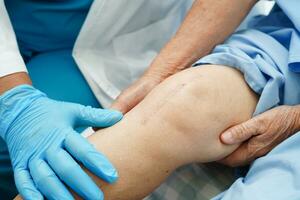 Arzt untersucht asiatische ältere Patientin mit Narben-Knieersatzoperation im Krankenhaus. foto