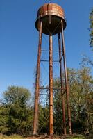 ein schön Wasser Turm ist einstellen um ein verlassen Bereich. diese rostig Metall Struktur steht hoch gegen ein Blau Himmel. foto