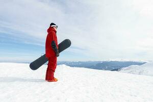 Snowboarder steht auf Hinterland Steigung und hält Snowboard. foto