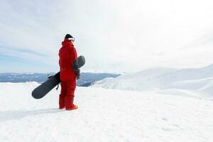 Snowboarder steht auf Hinterland Steigung und hält Snowboard. foto