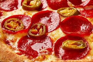 Nahansicht von Pizza mit Scheiben von Peperoni und Jalapenos auf geschmolzen Käse mit Tomate Soße foto
