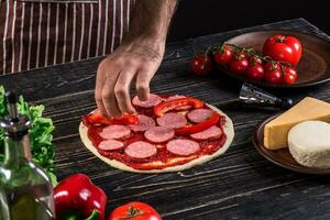 Koch im das Küche Putten das Zutaten auf das Pizza. Pizza Konzept. Produktion und Lieferung von Lebensmittel. foto