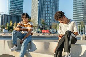 zwei glücklich Teenager freunde jeder einer suchen beim ihr Telefon im ein Bank im das Straße. foto