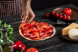 Koch im das Küche Putten das Zutaten auf das Pizza. Pizza Konzept. Produktion und Lieferung von Lebensmittel. foto