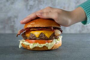 Frau Hand halten ein Hamburger mit Speck, Käse und Tomate foto