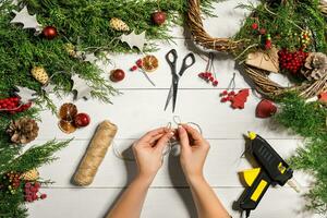 Weihnachten handgemacht DIY Hintergrund. Herstellung Kunst Weihnachten Kranz und Ornamente. oben Aussicht von Weiß hölzern Tabelle mit weiblich Hände. foto