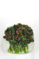 gebraten gekocht Grün Gemüse namens Kailan sind serviert auf ein Weiß Platte. isoliert auf solide Weiß Hintergrund foto