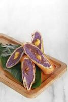 rollen lila Süss Kartoffel Kuchen serviert auf ein hölzern und Blatt Base mit ein Weiß Hintergrund foto