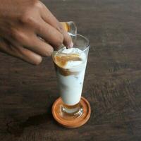 ein Barista gießt Kaffee Über Milch im ein klar Glas mit ein dunkel Hintergrund foto