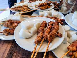 Hähnchen Satay mit Reis Kuchen serviert auf ein Weiß Teller und ordentlich vereinbart worden auf ein hölzern Tabelle foto