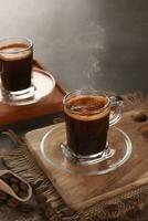 schwarz Kaffee ist serviert im ein klar Tasse mit ein hölzern Base foto
