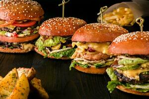 sortiert Burger mit anders Füllungen, mit Sesam Saat auf hölzern Tabelle isoliert auf schwarz Hintergrund. foto