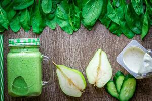 gesund Grün Smoothie mit Spinat im ein Becher gegen auf hölzern Hintergrund foto