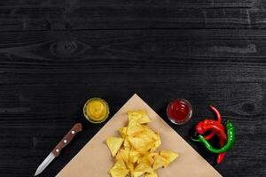 oben Aussicht von Tortilla Chips mit Soße und rot Chili Pfeffer auf schwarz hölzern Hintergrund foto