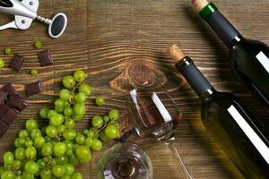 Flaschen und Brille von Wein, Schokolade und reif Trauben auf hölzern Hintergrund foto