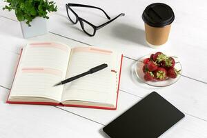 Büro Tabelle Schreibtisch mit einstellen von Lieferungen, Weiß leer Notizblock, Tasse, Stift, Tablette, Gläser, Blume auf Weiß Hintergrund. oben Aussicht foto