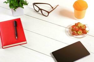 Büro Tabelle Schreibtisch mit einstellen von Lieferungen, rot Notizblock, Tasse, Stift, Tablette, Gläser, Blume auf Weiß Hintergrund. oben Aussicht foto