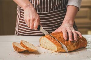 Frau Schneiden Brot auf hölzern Tafel. Backhaus. Brot Produktion. foto