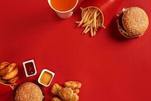 schnell Essen Gericht oben Sicht. Fleisch Burger, Kartoffel Chips und Glas von trinken auf rot Hintergrund. wegbringen Komposition. foto