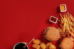 schnell Essen Gericht oben Sicht. Fleisch Burger, Kartoffel Chips und Glas von trinken auf rot Hintergrund. wegbringen Komposition. foto