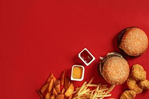 schnell Essen Gericht oben Sicht. Fleisch Burger, Kartoffel Chips und Nuggets auf rot Hintergrund. wegbringen Komposition. foto