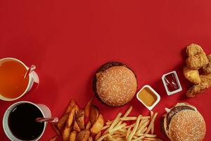 schnell Essen Gericht oben Sicht. Fleisch Burger, Kartoffel Chips und Glas von trinken auf rot Hintergrund. wegbringen Komposition. foto