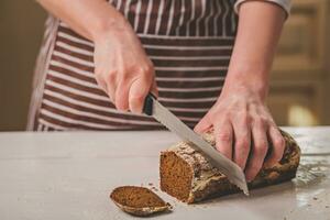 Frau Schneiden Brot auf hölzern Tafel. Backhaus. Brot Produktion. foto