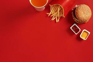 schnell Essen Gericht oben Sicht. Fleisch Burger, Kartoffel Chips und Glas von trinken auf rot Hintergrund. wegbringen Komposition. foto