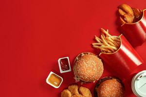 schnell Essen Gericht oben Sicht. Fleisch Burger, Kartoffel Chips und Glas von trinken auf rot Hintergrund. wegbringen Komposition. foto