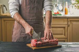 Mann schneidet von frisch Stück von Fleisch auf ein hölzern Schneiden Tafel im das Zuhause Küche foto