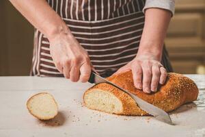 Frau Schneiden Brot auf hölzern Tafel. Backhaus. Brot Produktion. foto