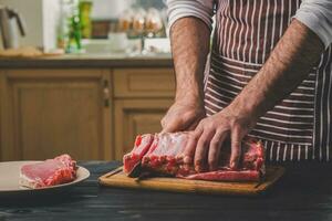 Mann schneidet von frisch Stück von Fleisch auf ein hölzern Schneiden Tafel im das Zuhause Küche foto